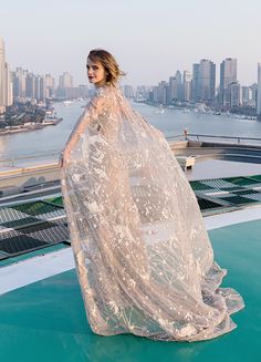 a woman is standing on top of a building wearing a long white dress with sheer sleeves