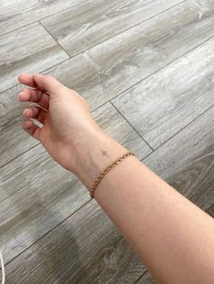 a person's arm with a small cross on it and a chain bracelet attached to the wrist