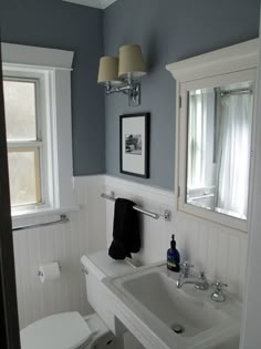 a white toilet sitting next to a sink in a bathroom under two windows with shades on them