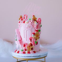 a pink birthday cake decorated with candy and candies on a gold stand in front of a pink wall