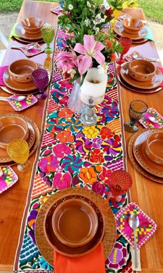 the table is set with plates, cups and vases on top of colorful cloth