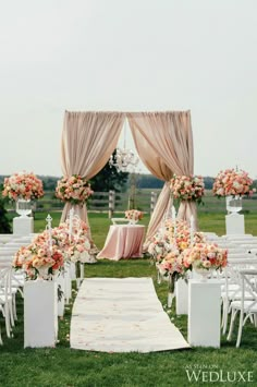 an outdoor wedding ceremony setup with white chairs and pink flowers on the aisle, chandelier draped over it