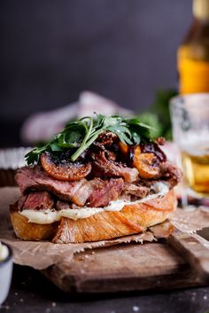 a sandwich with meat, cheese and spinach on a cutting board next to a glass of beer