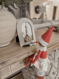 an elf doll sitting on top of a wooden table next to a bottle of liquid