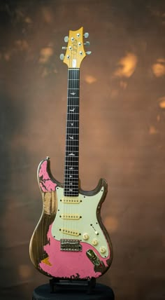 an electric guitar with pink and gold paint on it's body, sitting on a black stand