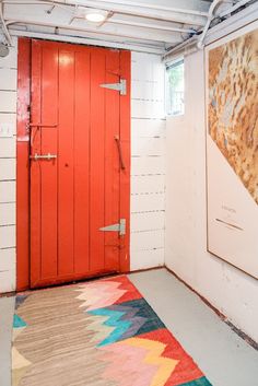 a red door in a white room with a colorful rug on the floor next to it