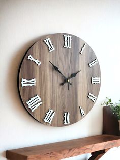 a wooden clock with roman numerals on the face is displayed against a white wall