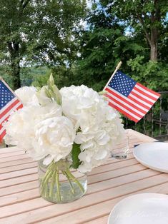 a vase filled with white flowers sitting on top of a wooden table next to plates