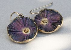 two purple flower shaped earrings are shown on a white surface