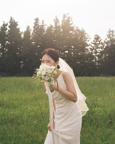 a woman in a white dress holding a bouquet of flowers and standing in the grass