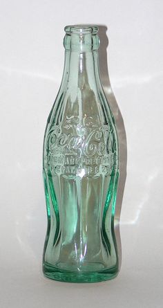 a green glass bottle sitting on top of a white table