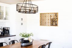 a dining room table and chairs in front of a white painted wall with gold accents