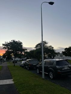 several cars parked in a parking lot next to a street light and trees at sunset