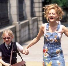 a woman walking down the street with a child holding her hand and wearing overalls