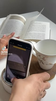 a person holding a cell phone next to an open book on top of a table