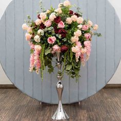 a silver vase filled with lots of flowers on top of a wooden floor next to a wall