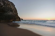 the sun is setting at the beach with waves coming in from the water and rocks on the shore