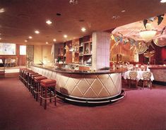 a bar with several stools and tables in a room that has red carpeted flooring