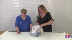 two women are standing at a table with some plastic bags