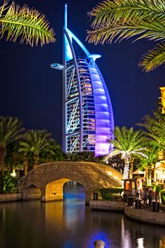 the bur is lit up at night with palm trees around it and lights reflecting in the water