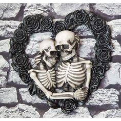 two skeletons sitting in front of a heart shaped frame with roses around them on a stone wall