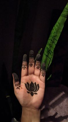 a person's hand with black and white tattoos on their fingers, holding up a green plant