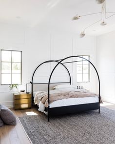 a bedroom with white walls and wood floors, an iron bed frame is in the center of the room