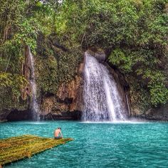 a man sitting on a raft in front of a waterfall with blue water and greenery