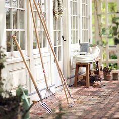 two garden tools leaning up against the side of a house with potted plants in it