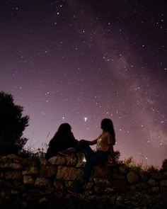 two women sitting on a stone wall under the night sky