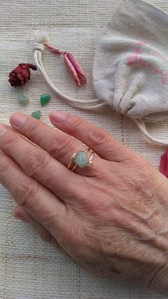 an older woman's hand holding a ring with green stones and other items surrounding it