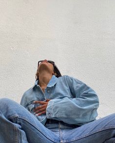 a person sitting on the ground with their head in his hands, wearing jeans and a denim jacket