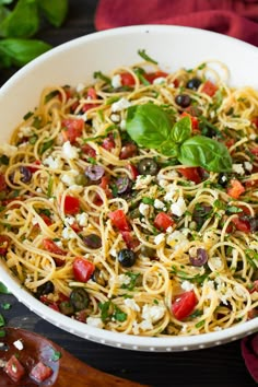 a white bowl filled with pasta and vegetables on top of a wooden cutting board next to basil leaves