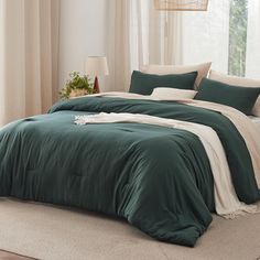 a bed with green comforter and pillows in a room next to a large window