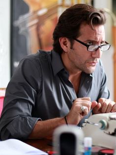 a man sitting at a table with a sewing machine in front of him and looking down