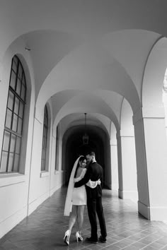 a bride and groom standing in an arched hallway with their arms wrapped around each other