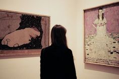 a woman standing in front of two paintings on display at an art gallery with her back turned to the camera