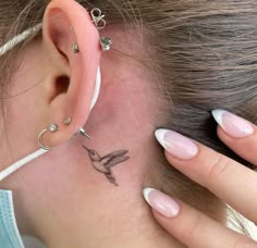 a woman has a small humming tattoo on her behind the ear and behind the ear is a tiny bird