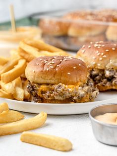 a cheeseburger and fries on a plate with some dipping sauce in the background