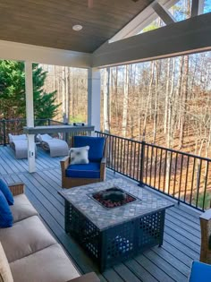 a covered deck with blue chairs and a fire pit in the middle, surrounded by trees