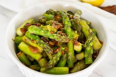 a white bowl filled with asparagus on top of a marble counter next to lemon wedges