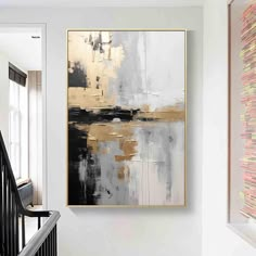 an abstract painting hangs on the wall next to a stair case with black and gold accents