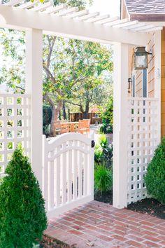 a white gate and brick walkway leading to a house with trees in the back yard