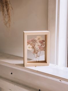 a wooden frame with flowers in it sitting on a window sill