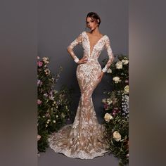 a woman in a long sleeved wedding dress standing next to flowers and greenery