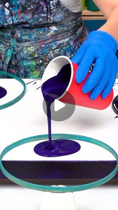 a person in blue gloves pours purple liquid into a cup on top of a table