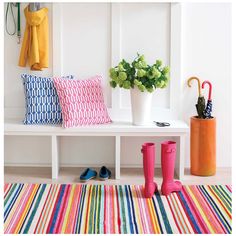 a white bench with colorful striped rugs and rain boots on it next to a potted plant