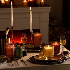 a table topped with candles and plates filled with wine glasses next to a fire place