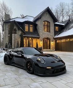 a black sports car parked in front of a large house with snow on the ground