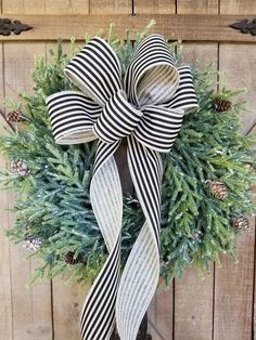 a black and white christmas wreath with pine cones, evergreens and striped ribbon hanging on a wooden door